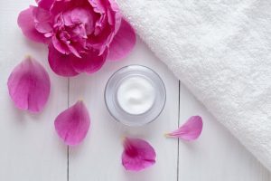 What is Retinol Represented by Glass Jar of Anti-Aging Cream Surrounded by Fuschia Flowers and Petals on White Wooden Surface | Vitacost.com/blog
