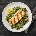 Top View of Grilled Fish Over Greens on White Plate Black Table | Vitacost Blog