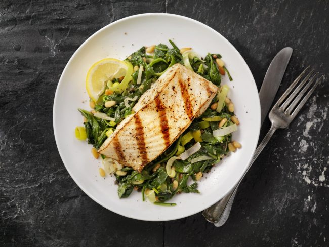 Top View of Grilled Fish Over Greens on White Plate Black Table | Vitacost Blog