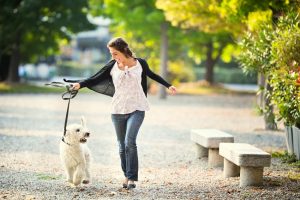 Woman Learning How to Boost Energy to Beat the Afternoon Slump Walking White Dog in Park | Vitacost.com/blog