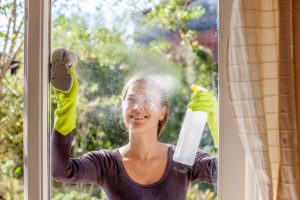 Woman in Green Gloves Doing Fall Cleaning Spraying Outside of Home Windows With Cleaner and Wiping with Cloth | Vitacost.com/blog