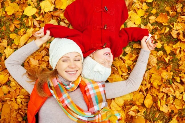 Mother and Daughter Lying in Freshly Raked Pile of Yellow Leaves as They Enjoy Fall Activities Together as a Family | Vitacost.com/blog