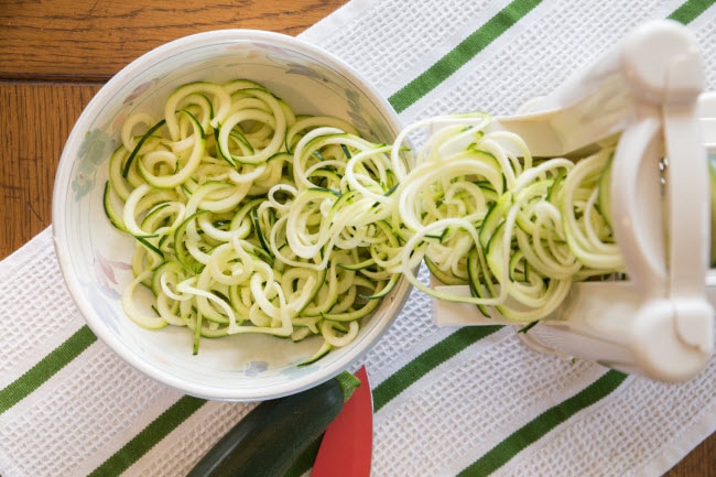 Overhead View of Zucchini Being Spiralized into Bowl on Green-and-White Striped Towel as Example of Keeping a Healthy Diet Interesting | Vitacost.com/blog