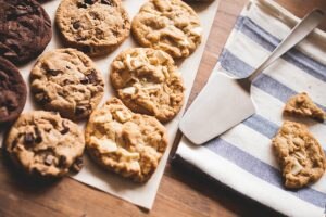How to Make Healthy Cookies Represented by Rows of Various Homemade Cookies on Parchment Paper and Towel with Serving Utensil | Vitacost.com/blog
