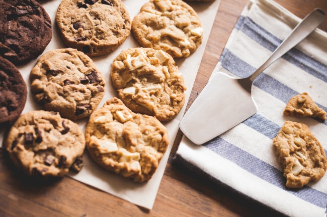 How to Make Healthy Cookies Represented by Rows of Various Homemade Cookies on Parchment Paper and Towel with Serving Utensil | Vitacost.com/blog