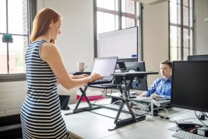 Red-Haired Woman in Striped Dress Enjoying Standing Desk Benefits at Work | Vitacost.com/blog