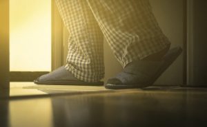 Pajama-Clad Person in Slippers Who Needs Solutions for How to Stop Urinating at Night Shuffling to Bathroom Through Dimly Lit Hallway | Vitacost.com/blog