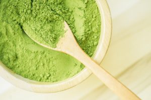 Overhead View of Bright Green Plant-Based Protein Powder in Light Brown Wooden Bowl With Wooden Spoon Rested on Top | Vitacost.com/blog