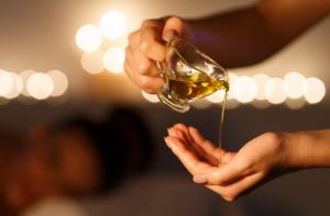 DIY Body and Massage Oil Made with Essential Oils Being Poured From Small Glass Pitcher into Woman's Hand | Vitacost.com/blog