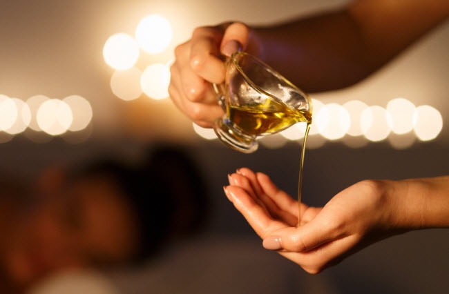 DIY Warming Chai Body and Massage Oil DIY Body and Massage Oil Made with Essential Oils Being Poured From Small Glass Pitcher into Woman's Hand | Vitacost.com/blog
