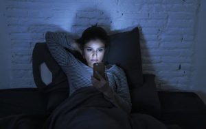 Woman in Bed at Night Staring at Smartphone Possibly Experiencing Premature Aging From the Effects of Blue Light From the Screen | Vitacost.com/blog