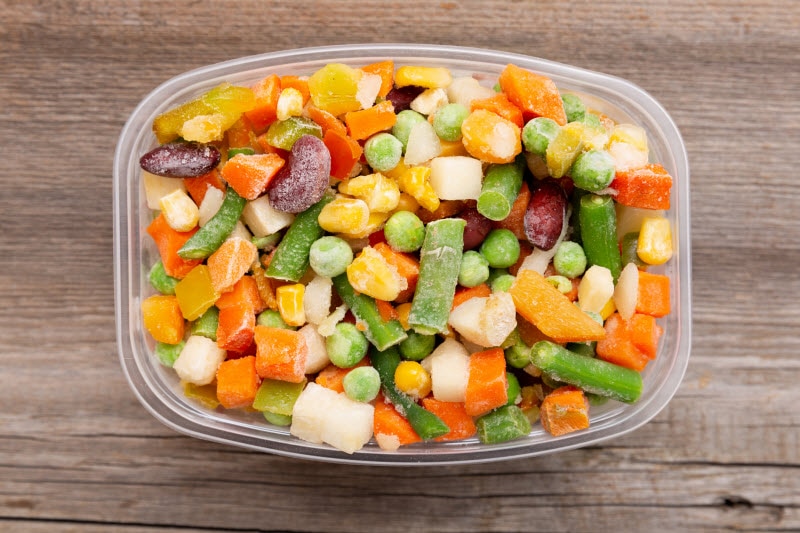 Concept of Fresh vs Frozen Fruit and Vegetables Represented by Container Filled With Frozen Vegetables and Beans on Wooden Table | Vitacost.com/blog