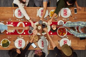 Overhead View of Holiday Food-Filled Table With Arms of Those Gathered Around Toasting Glasses Before Excessive Eating Begins | Vitacost.com/blog