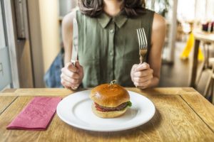 Torso View of Woman Not Concerned About the Health Effects of Eating Red Meat About to Dig Into a Burger at a Restaurant | Vitacost.com/blog