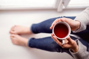 Concept of Tea for Brain Health Benefits Represented by Woman in Jeans and Sweater Sitting on Floor Holding Cup of Tea | Vitacost.com/blog