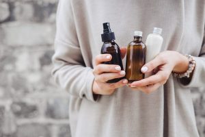 Torso View of Woman in Gray Sweater Holding Various Bottles to Represent Concept of Skincare Ingredients | Vitacost.com/blog