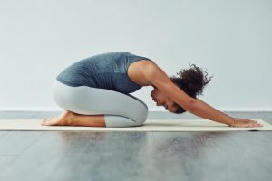 Woman Who Experimented with Different Types of Yoga Executing Perfect Child's Pose on Cream-Colored Yoga Mat on Wooden Floor | Vitacost.com/blog