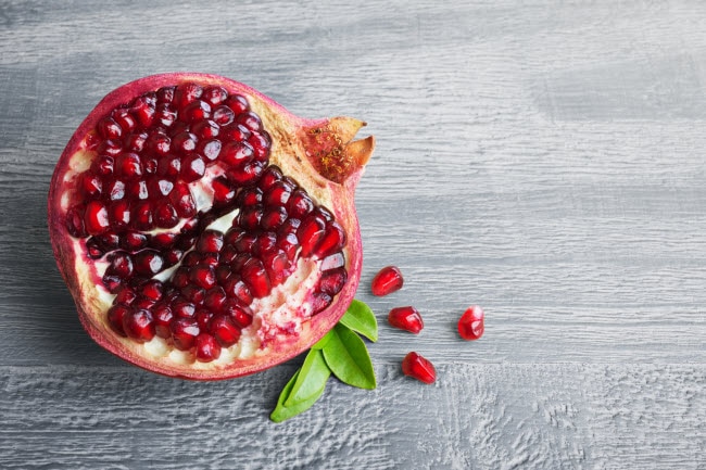 Cut-Open Pomegranate With Seeds Spilling Out on Gray Table Surface  as Example of Top Superfoods to Add to Your Diet  | Vitacost.com/blog