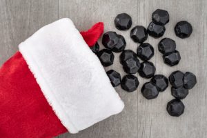Concept of Charcoal Beauty Products as Stocking Stuffers Represented by Black Coal Pieces Spilling From Red and White Christmas Stocking on Wood Surface | Vitacost.com/blog