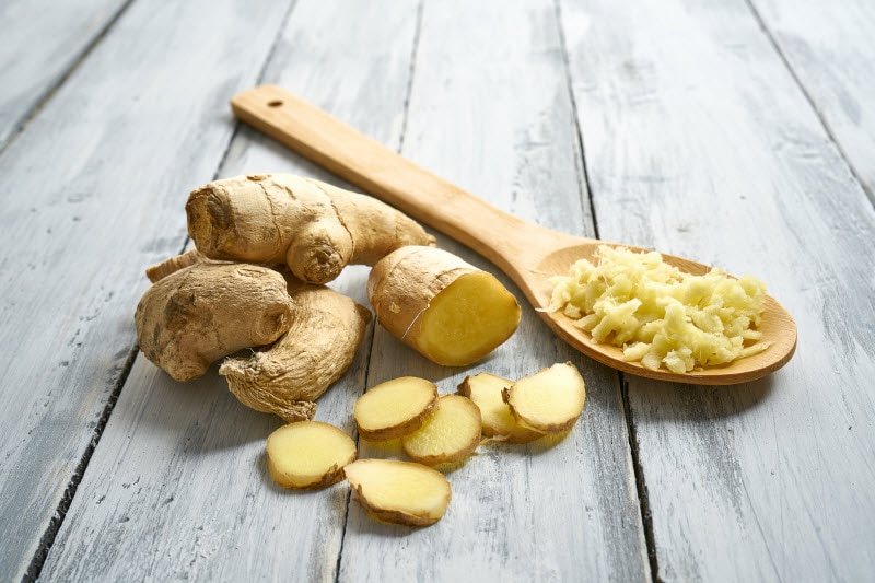 Fresh Ginger Sliced and Grated on Wooden Spoon on Gray Wood Surface to Represent Concept of the Health Benefits of Ginger | Vitacost.com/blog
