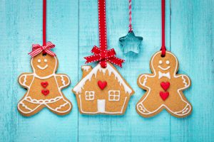 Festive Gingerbread-Shaped Homemade Cinnamon Ornaments Hanging From Red Ribbon Against Teal Blue Wooden Background | Vitacost.com/blog