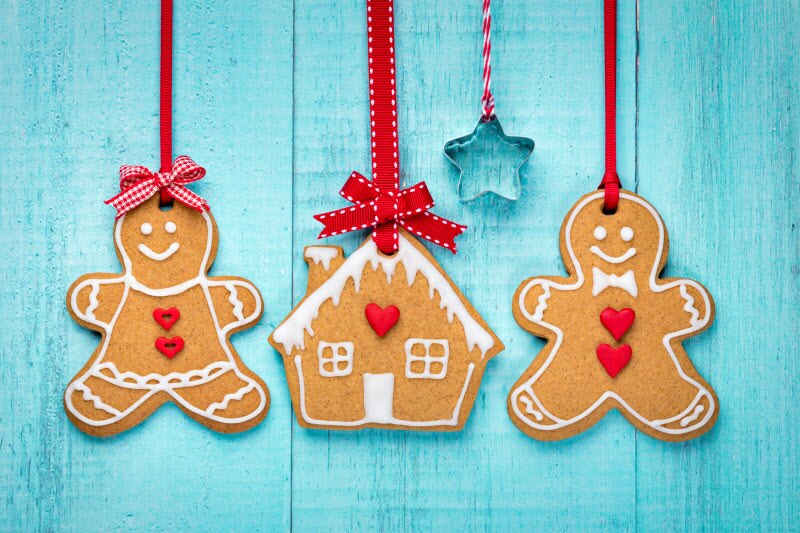 Festive Gingerbread-Shaped Homemade Cinnamon Ornaments Hanging From Red Ribbon Against Teal Blue Wooden Background | Vitacost.com/blog