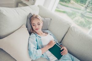 Young Blonde-Haired Woman Who Discovered the Ideal Nap Length Snoozing on White Couch in Afternoon | Vitacost.com/blog