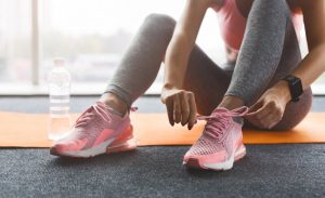 Woman Focused on Reaching Fitness Goals Tying Sneakers While Seated on Orange Mat at the Gym | Vitacost.com/blog
