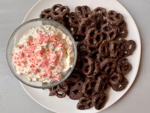 Peppermint cheesecake dip in bowl with chocolate covered pretzels on plate