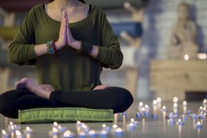 Woman Sitting on Green Mat Surrounded by Candles in Dimly Lit Room Practicing Mindfulness Meditation | Vitacost.com/blog