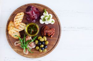 Example of How to Follow the Mediterranean Diet Including Round Wooden Platter Filled with Olives, Oil, Sundried Tomatoes, Meats & Cheese | Vitacost.com/blog