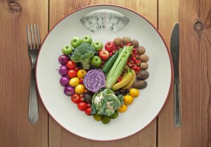 Plate With Scale Setting Filled with Fruits & Veggies in Heart Shape on Wood Table to Represent Concept of How to Prevent Obesity | Vitacost.com/blog