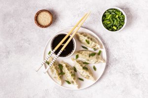 Top View of Pot Stickers on White Plate With Dipping Sauce, Sesame Seeds and Green Onions | Vitacost Blog
