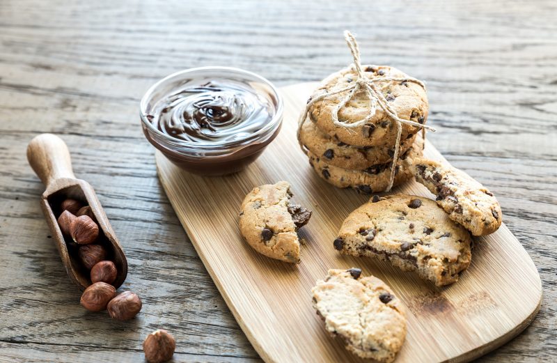 Chocolate Chip Cookies Stuffed with Chocolate Sauce Next to Hazelnuts on Cutting Board | Vitacost Blog