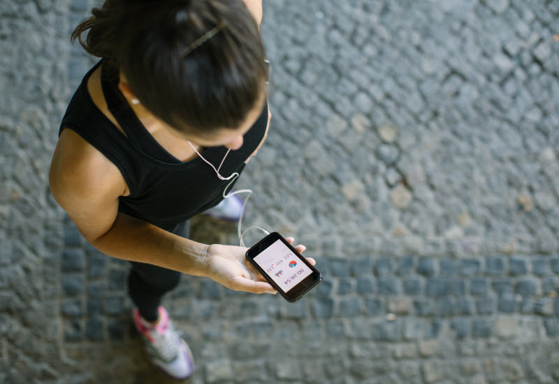 Overhead View of Woman in Black Workout Gear and Sneakers Looking at Best Fitness Apps on Her Mobile Phone | Vitacost.com/blog