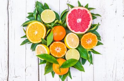 Benefits of Citrus Fruits Represented by Variety of Halved Oranges, Lemons and Grapefruit in Heart Shape with Green Leaves on White Wood Surface | Vitacost.com/blog