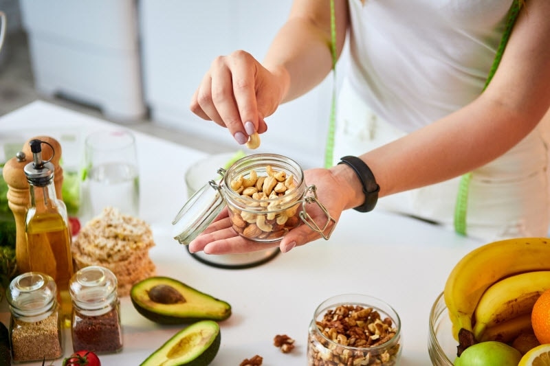 Woman Trying Keto Snack Ideas Filling Small Jars with Assorted Nuts | Vitacost.com/blog