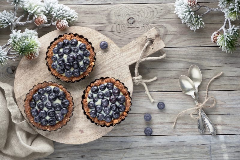 Top View of Blueberry Tarts on Cutting Board Surrounded by Winter-Inspired Pine Tree Decorations | Vitacost Blog