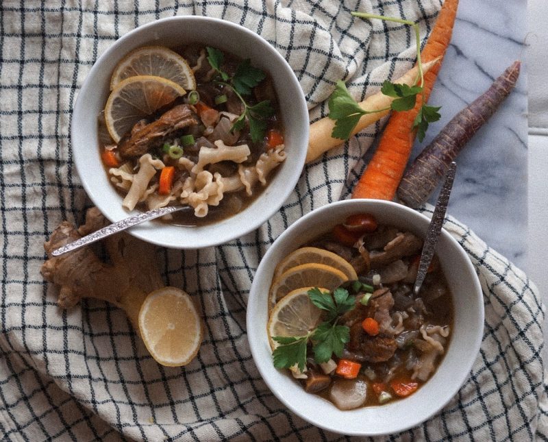 Top View Two Bowls of Loaded Chicken Noodle Soup Next to Fresh Veggies | Vitacost Blog