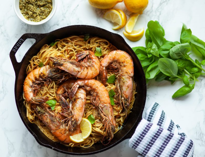 Top View of Iron Skillet Filled with Pasta and Prawns Next to Fresh Herbs | Vitacost Blog