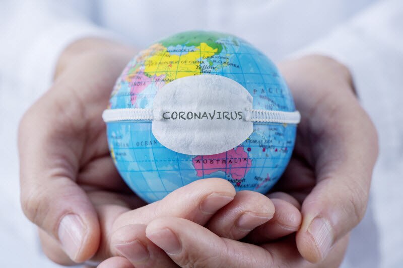 Mini Globe With White Mask Around it in Person's Cupped Hands to Represent Information About Coronavirus | Vitacost.com/blog