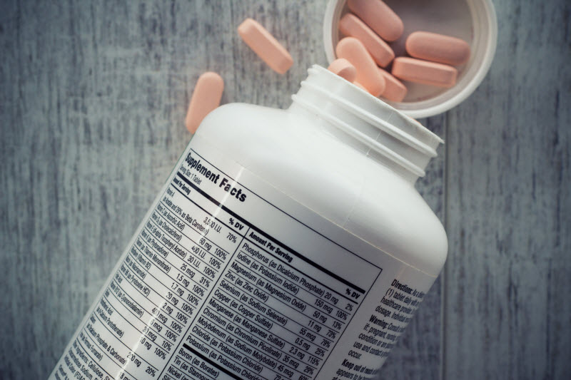 Multivitamin Ingredients Represents by Open Bottle of Supplements With Tablets Spilling Out on Wooden Table | Vitacost.com/blog