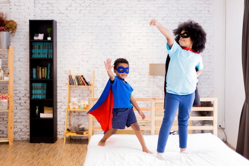 Two Children In Superhero Costumes Acting Out Skit in Bedroom to Represent Creative Activities for Kids | Vitacost.com/blog