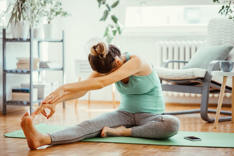 Woman on Living Room Floor Doing Quick Stretching Routine to Reset | Vitacost.com/blog