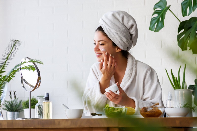 Woman in Robe with Towel on Head Applying Cream to Face to Represent What is the Best Skincare Routine for Every Decade | Vitacost.com/blog