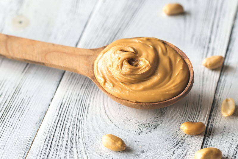 Wooden Spoon with Peanut Butter on White Wood Surface to Represent Different Types of Nut Butter | Vitacost.com/blog