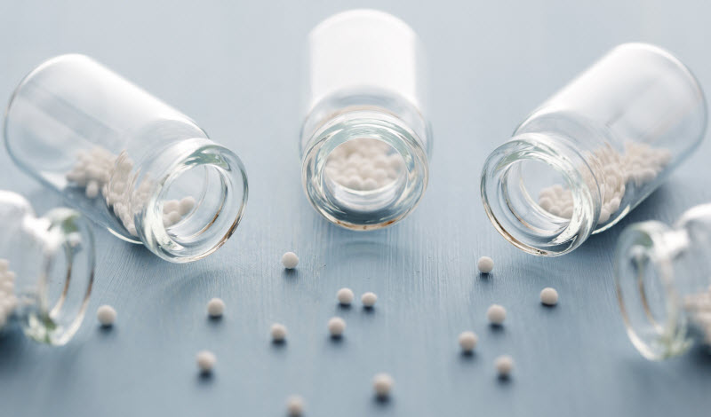 Clear Bottles Spilling Out White Pellets on Blue Wood Surface to Represent Natural Remedies to Boost Immune Health | Vitacost.com/blog