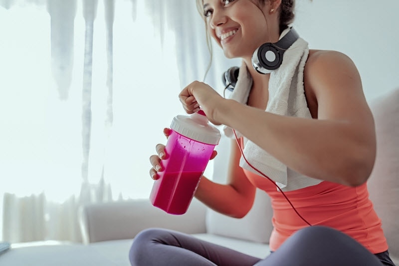 Smiling Woman in Workout Gear Drinking Smoothie From Pink Bottle After Learning How to Create a Diet Plan to Match Her Fitness Routine | Vitacost.com/blog