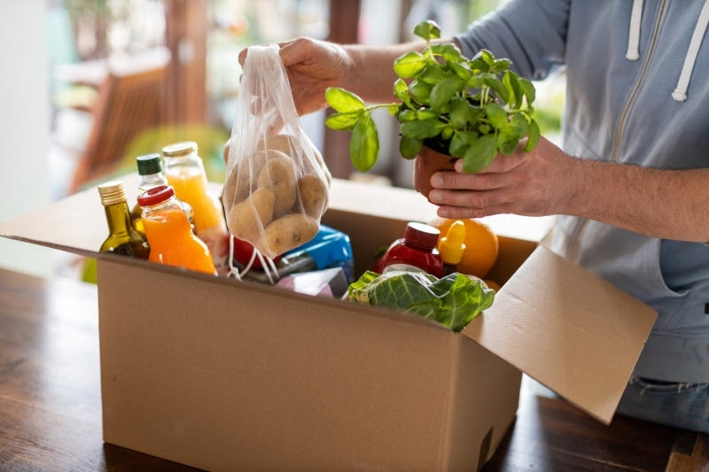 Man Unpacking Food From Delivery Box as Example of How to Grocery Shop During the Pandemic | Vitacost.com/blog