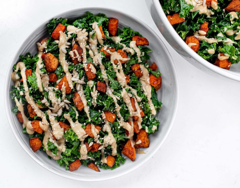 Top View Sweet Potato and Kale Salad Drizzled with Dressing in White Bowl on White | Vitacost Blog